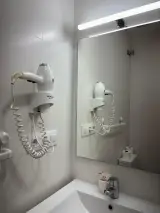 Primer plano del secador de pelo de pared junto al espejo y el lavabo con neceser del baño